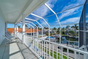 A covered balcony with white railings, overlooking a marina with boats and palm trees.