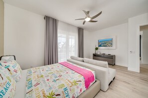 Ein modernes Schlafzimmer mit Bett, Sofa, Deckenventilator, Fernseher und einem Fenster mit Vorhängen.