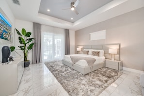 A modern bedroom with a large bed, a ceiling fan, a TV, and a potted plant.