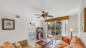 Una sala de estar con sofá, sillones, una mesa de centro, televisor y ventilador de techo.