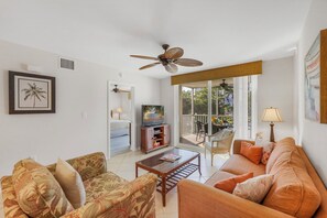 A living room with a sofa, armchairs, a coffee table, a television, and a ceiling fan.