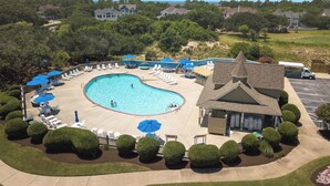 Una piscina amb gandules i ombrel·les, envoltada de brosses ben cuidades i un edifici amb teulada a dos vessants.