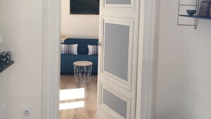 Ein Flur mit einer weißen Tür, die zu einem Raum mit einem blauen Sofa und einem Gemälde an der Wand führt.