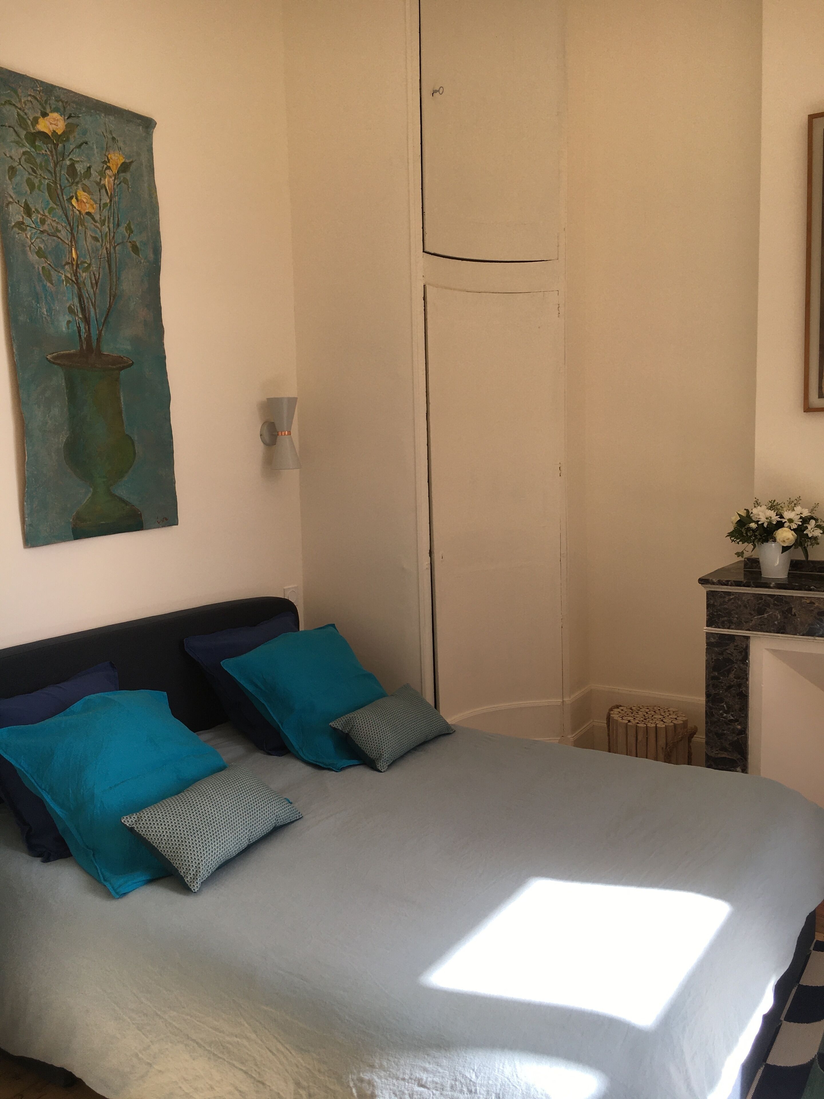 A bedroom with a bed, two pillows, a nightstand, a painting, and a window.
