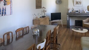 Ein Essbereich mit einem langen Tisch, Holzstühlen, einem Fernseher und einem Kamin.