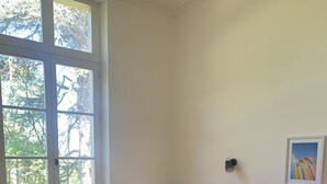 Ein Schlafzimmer mit einem großen Fenster, einem Bett mit rosa Bettwäsche, einem gestreiften Sessel und einer Bank mit Handtüchern.