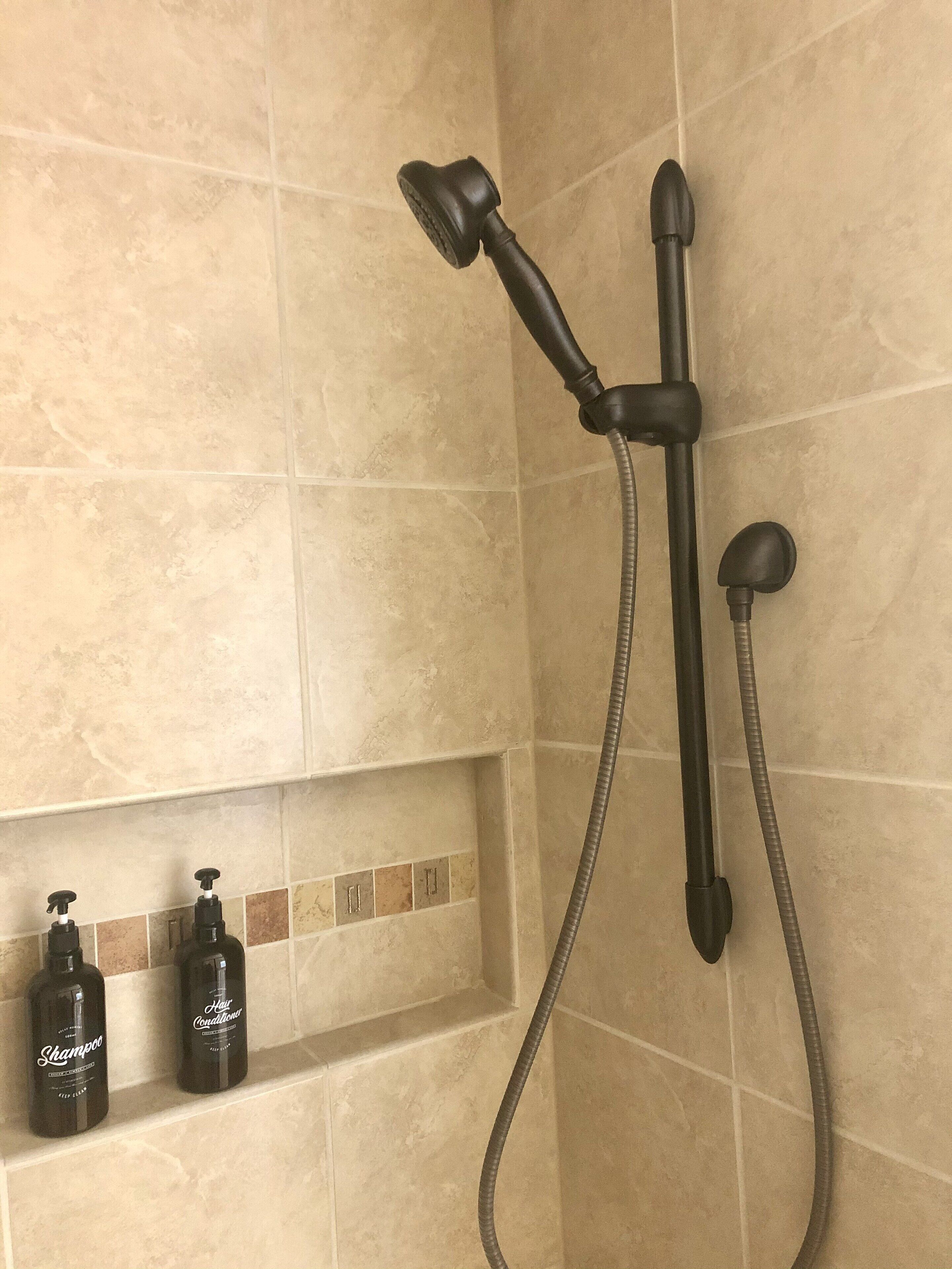 La douche est équipée d’un pommeau de douche à main et d’un pommeau fixé au mur. Deux flacons de shampoing et d’après-shampoing sont posés sur le mur.