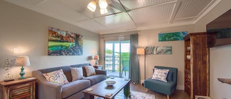 A living room with a sofa, coffee table, and a cabinet. There is a ceiling fan, a window with curtains, and a painting on the wall.