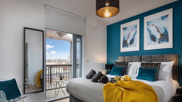 A modern bedroom with a large bed, a balcony with a city view, and abstract art on the wall. - Plymouth Sea-View PENTHOUSE-Habita Property (England)