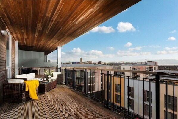 A balcony with wooden flooring, wicker furniture, and a yellow throw blanket.