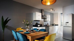 A modern kitchen with white cabinets, a wooden dining table, and blue chairs. - Plymouth Sea-View PENTHOUSE-Habita Property (England)