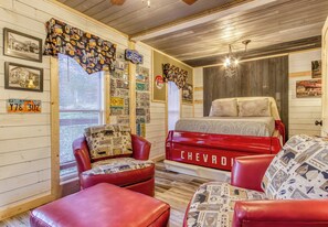 A room with a bed, red leather chairs, and a red Chevrolet truck bed as a headboard.