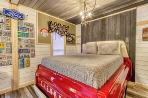 A bedroom with a vintage Chevrolet bed, wooden walls, and a chandelier.