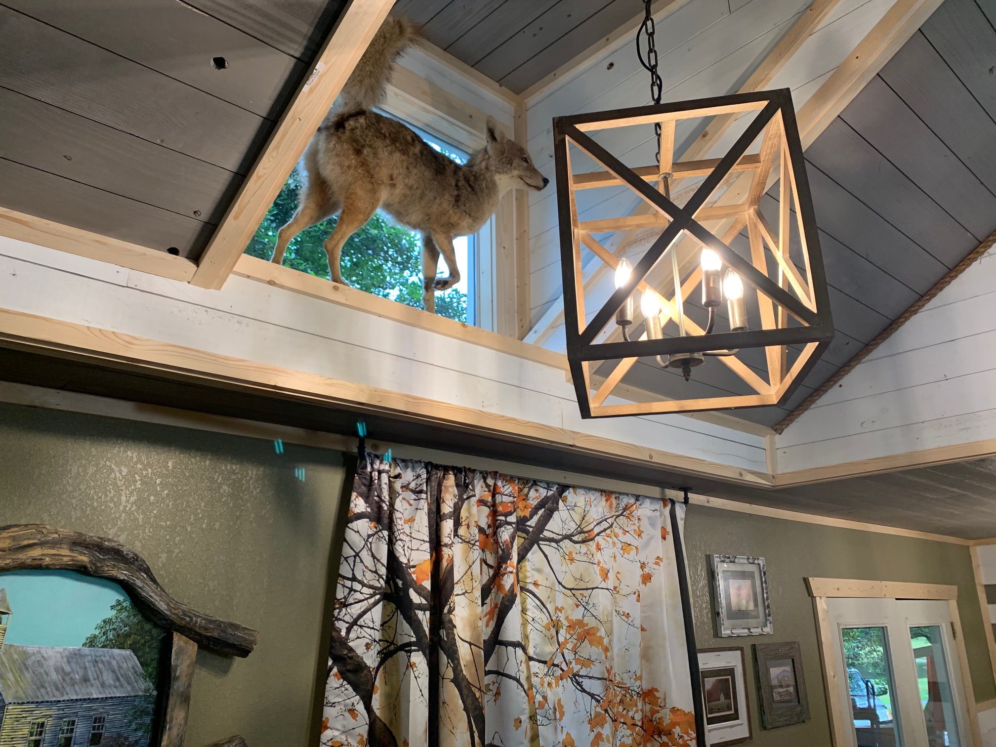 A rustic interior with a wooden ceiling, a hanging lantern, and a deer visible through a window.