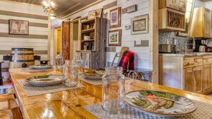 A rustic kitchen with wooden cabinets, a wooden dining table set with plates, and a chandelier.