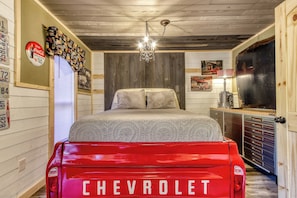 A bedroom with a Chevrolet truck bed as a bed, a chandelier, and a dresser with drawers. - Fire-Pit | Hot Tub | WiFi | Pet Friendly | Arcade | Close to Attractions (Sevierville)