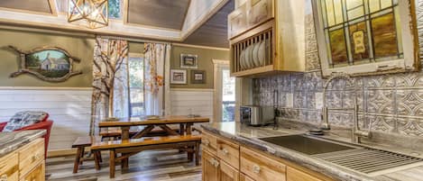 A rustic kitchen with wooden cabinets, a stone countertop, and a hanging light fixture.
