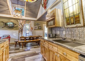 A rustic kitchen with wooden cabinets, a stone countertop, and a hanging light fixture.