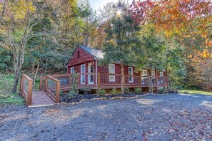 A wooden cabin with a covered porch and a gravel driveway, surrounded by autumn foliage. - Fire-Pit | Hot Tub | WiFi | Pet Friendly | Arcade | Close to Attractions (Sevierville)