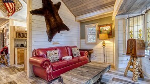 A cozy interior with a red leather sofa, a mounted bear hide, wooden flooring, and a rustic wooden coffee table.