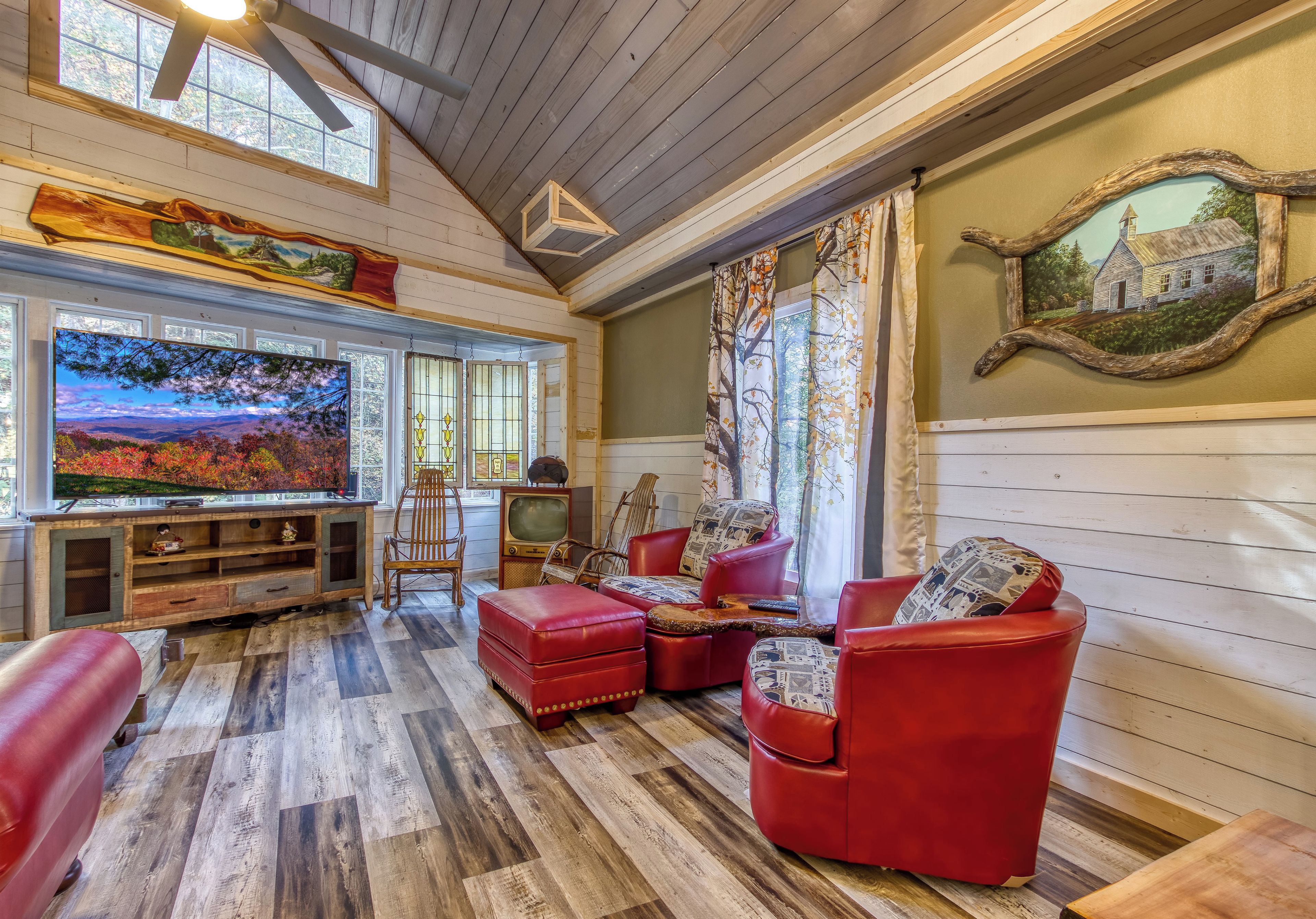 A cozy living room with a large flat-screen TV, red leather furniture, and a wooden ceiling.