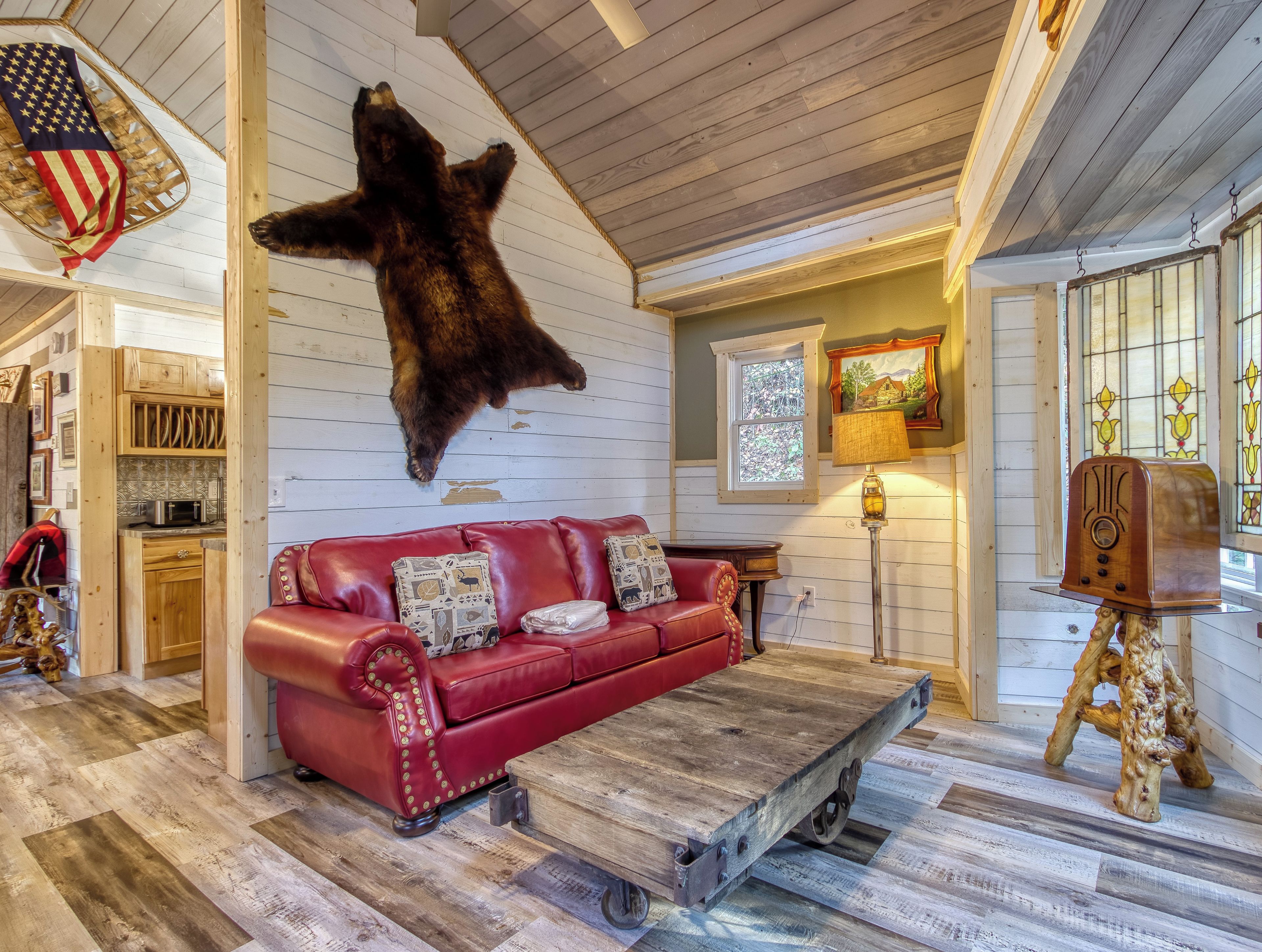 A cozy interior with a red leather sofa, a mounted bear hide, wooden flooring, and a rustic wooden coffee table.