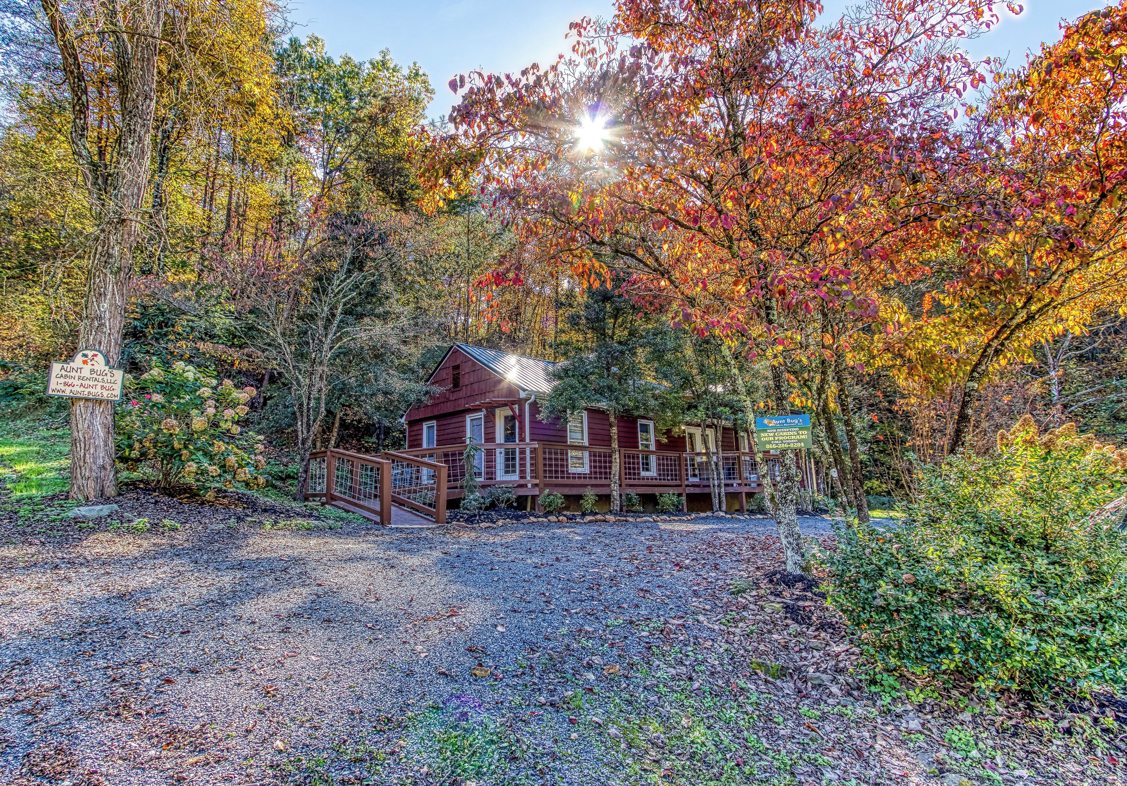 A cabin with a wooden deck and a gravel driveway.