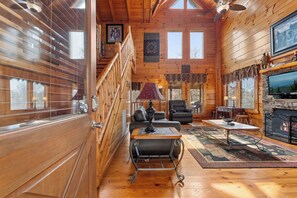 A wooden cabin interior with a staircase, a fireplace, a television, and a dining area.