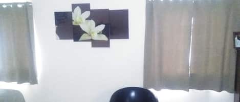 A room with a bed, a black chair, a wall-mounted decoration, and two curtains.