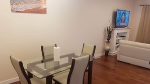 A dining area with a glass table and chairs, a television on a stand, and a sofa in a living room. - Stylish Heritage Apt Ideal For Long Stays - 3 BR with Jacuzzi (Fort McMurray)