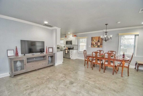 A spacious living area with a large flat-screen TV, wooden dining table, and chairs.