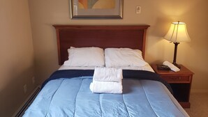 Un llit ben fet amb un llençol blau i nínxols blancs, una tovallola doblegada sobre el llit, una làmpada de nit i un quadre abstracte emmarcat a la paret.