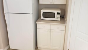 A compact kitchen with a white refrigerator and microwave on a countertop. - 3 Bedroom Furnished Apartment  suitable for Company Staff with Large Yard  Space (Fort McMurray)