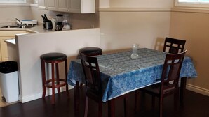 A dining area with a table covered by a blue tablecloth, four wooden chairs, a vase on the table, and a kitchen area with a sink and cabinets in the background. - 3 Bedroom Furnished Apartment  suitable for Company Staff with Large Yard  Space (Fort McMurray)