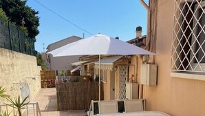 A patio area with a table and chairs, a white umbrella, and potted plants.