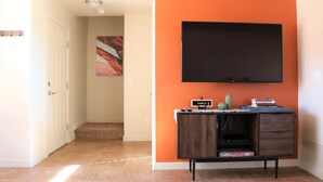 A hallway with a TV mounted on an orange wall, a small cabinet with a cactus, and a door leading to another room. - 18A4 Moab Adventure! Pool with Red Rock Views (MOAB)