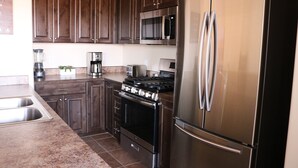 A kitchen with dark wooden cabinets, stainless steel appliances including a refrigerator, microwave, and stove, and a granite countertop. - 18A4 Moab Adventure! Pool with Red Rock Views (MOAB)