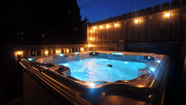 Un jacuzzi iluminado, rodeado por una cerca de madera.