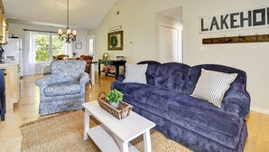 Una sala de estar con un sofá azul, un sillón estampado, una mesa de centro blanca y un comedor al fondo.