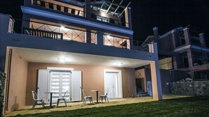 Een tweelaags gebouw met een overdekte patio, compleet met een tafel, stoelen, een deur en een raam met luiken.