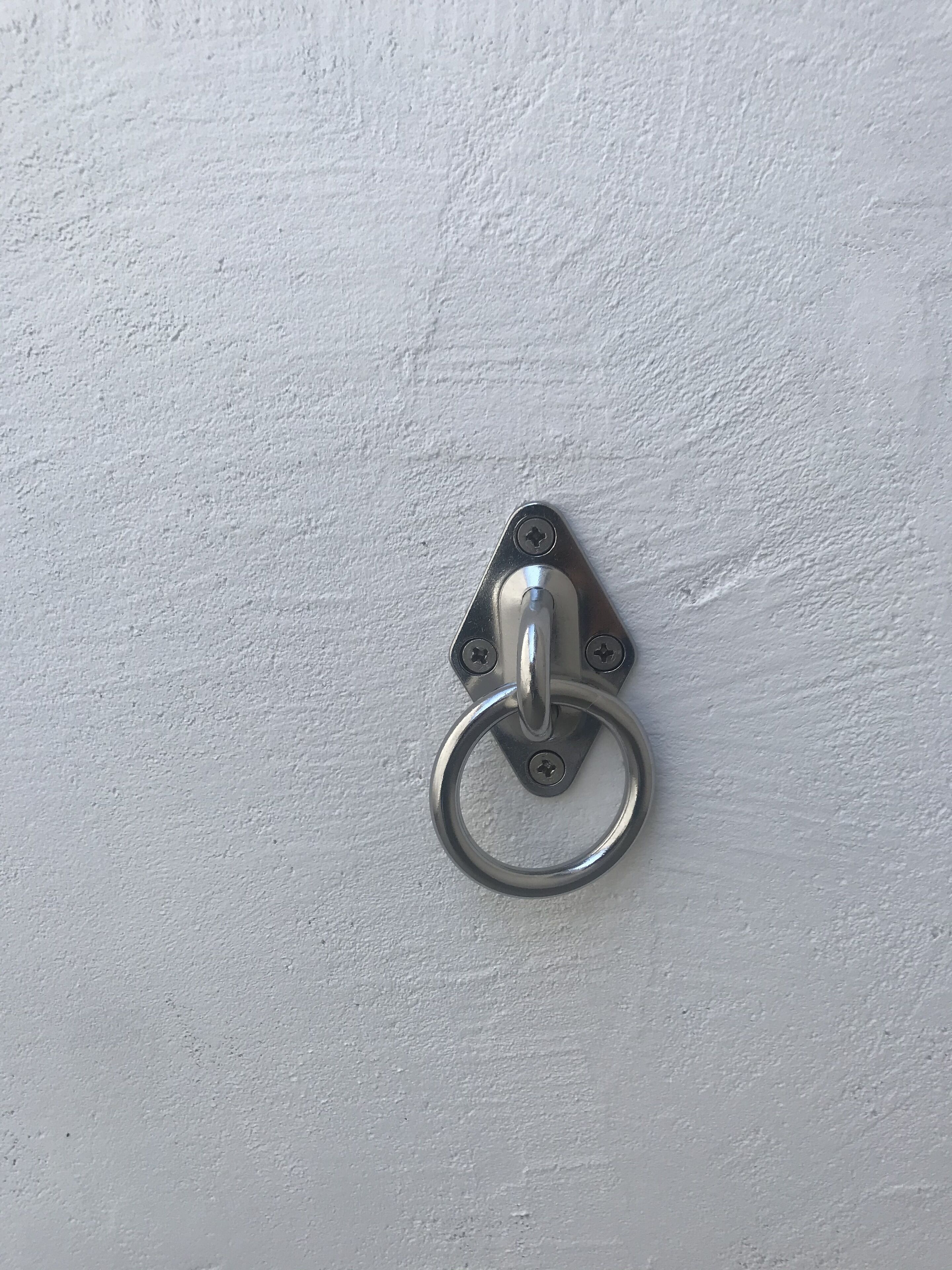 A metal door knocker mounted on a white textured wall.