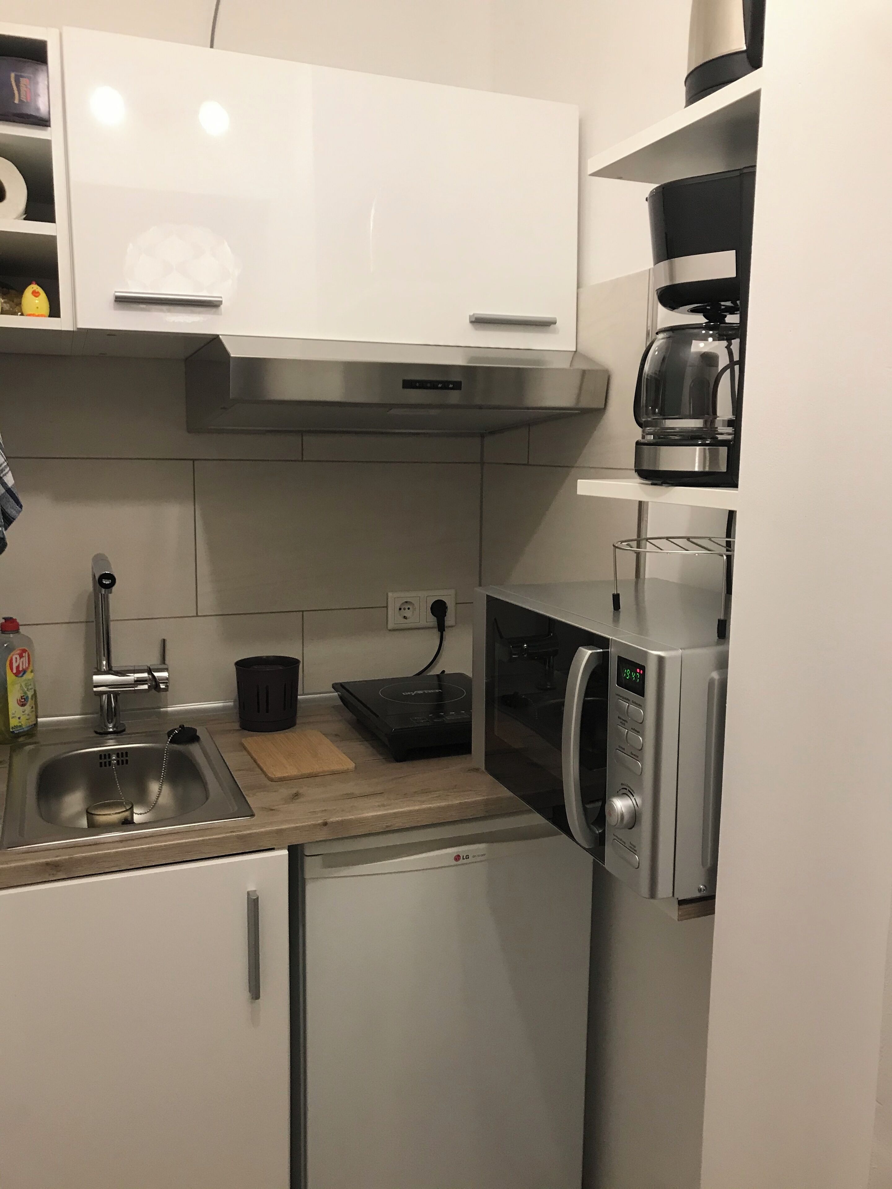 A compact kitchen with a stainless steel sink, a coffee maker, and a microwave.