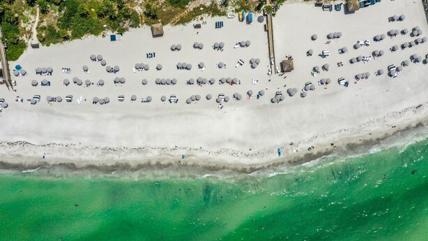 An aerial view of a beach with rows of sun loungers and umbrellas, a pier extending into the water, and clear turquoise sea. - Longboat Key Club!! Direct Beachfront!! (Longboat Key)