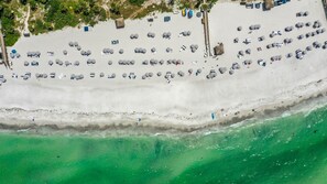 Luchtbeeld van een strand met rijen ligbedden en parasols, een pier die het water in reikt, en heldere turquoise zee.