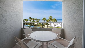 A balcony with a round table and chairs, overlooking a beach with palm trees and a clear sky. - Longboat Key Club!! Direct Beachfront!! (Longboat Key)