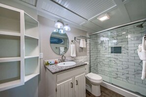 A bathroom with a glass shower enclosure, a white sink, and a mirror above it.