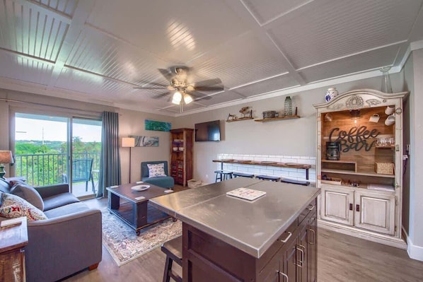 A spacious living area with a large island, a sofa, and a balcony with a view.