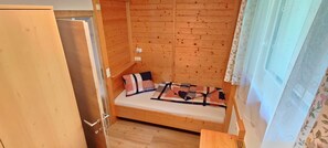 A small wooden room with a bunk bed, a door, and a window with floral curtains. - Wohnung Ost - Haus Lukasser (Kosten)