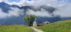 A mountain landscape with a church, a path, and a building. - Wohnung Ost - Haus Lukasser (Kosten)