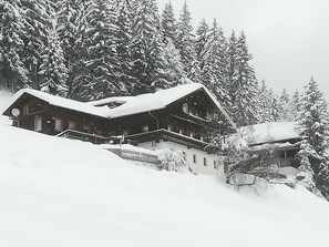 A snow-covered lodge with a prominent central structure, surrounded by dense forest. - Wohnung Ost - Haus Lukasser (Kosten)